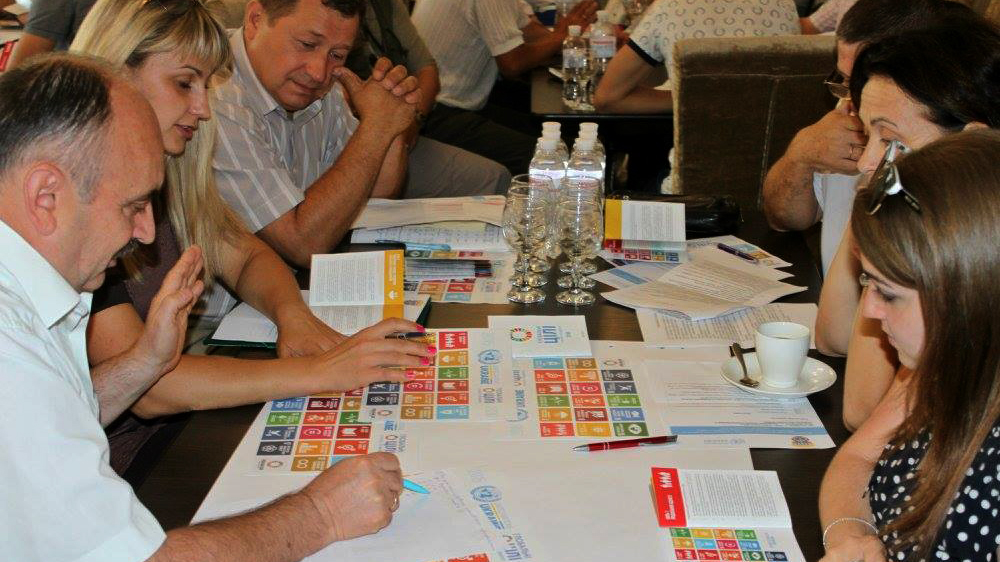 Photo: UNO Kyiv Group of people sitting around a desk looking at SDG brochures