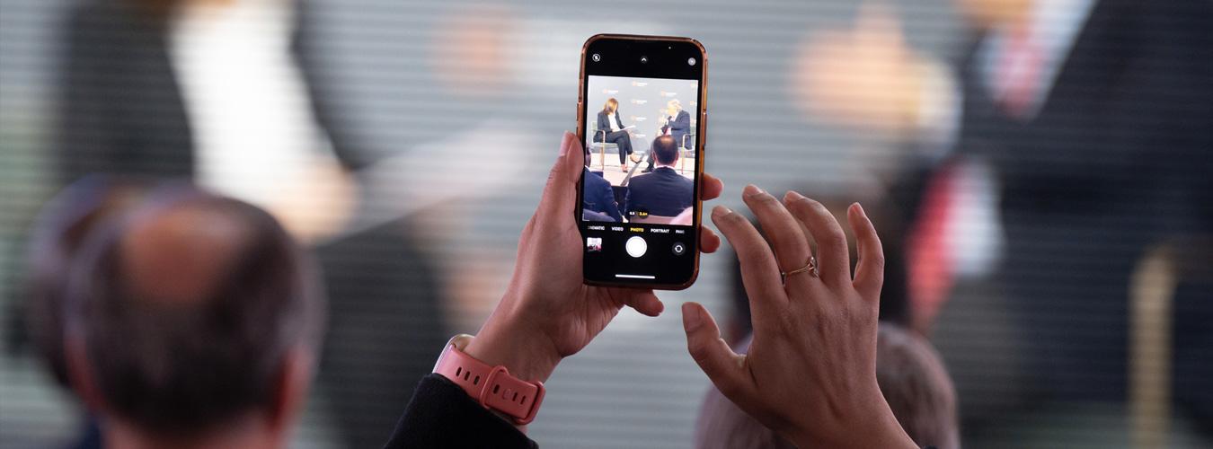 Hands holding a phone up to take a photo of panelists in discussion