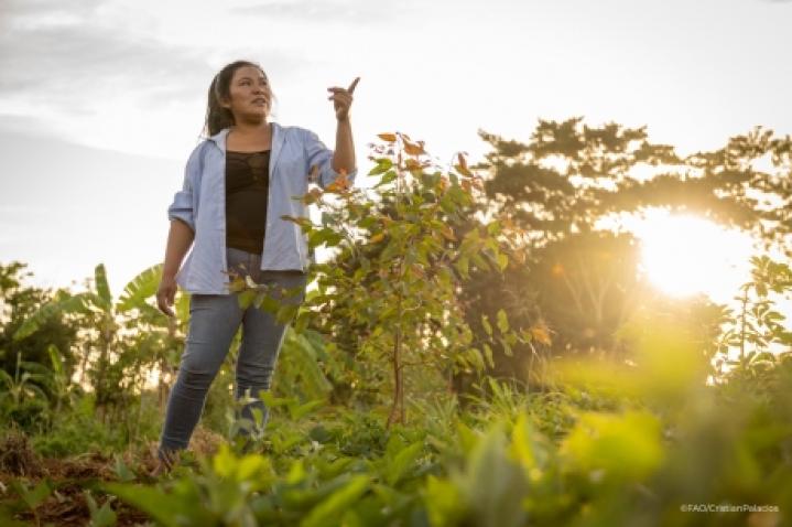 A woman working in the field points at something out of frame 